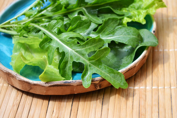 Summer mix of vegetables spinach arugula salad in blue plate on wooden surface