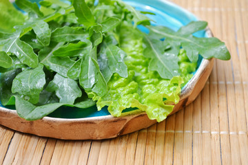Summer mix of vegetables salad arugula spinach in blue plate on wooden surface