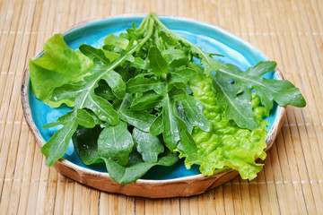 Summer mix of vegetables arugula salad spinach in blue plate on wooden surface