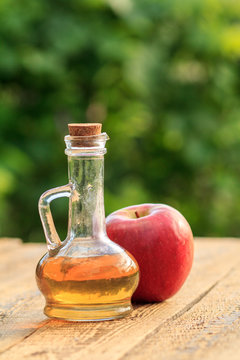 Apple vinegar in glass bottle with cork and fresh red apple on old wooden boards with blurred green natural background. Organic food for health