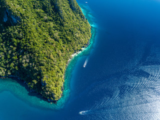Aerial drone view down onto boats over a tropical coral reef surrounded by mountains and jungle