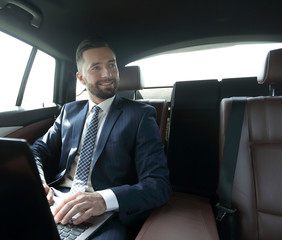 man with laptop sitting in the back seat in the car