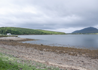 Beautiful beach, with mountains in the background and cloudy skies, with forest along the coast. Taken in Letterfrack along the Wild Atlantic Way, Ireland in summer.