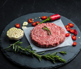 Raw ground beef meat burger steak cutlet with chili, rosemary and garlic on black slate plate for cooking
