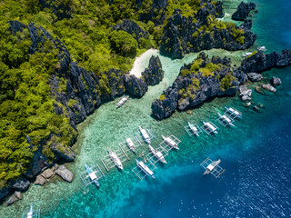 Aerial drone view of large numbers of tourist boats next to a tropical lagoon and beach in El Nido, Palawan
