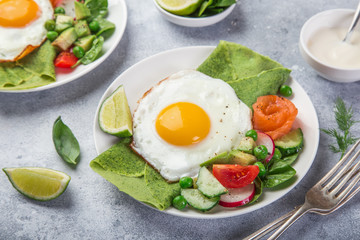 green spinach crepes with fried eggs, smoked salmon and vegetables for breakfast
