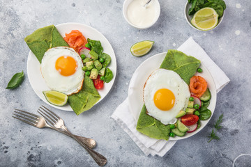 green spinach crepes with fried eggs, smoked salmon and vegetables for breakfast