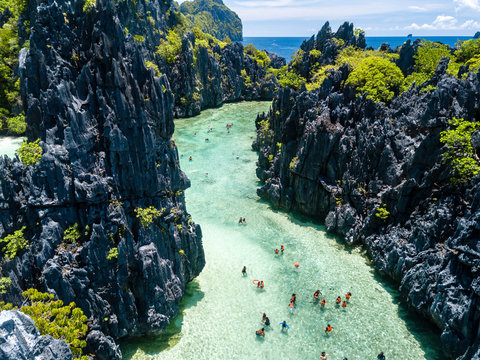 Aerial drone view of swimmers and tourists inside a beautiful, shallow tropical laggon surrounded by jagged cliffs