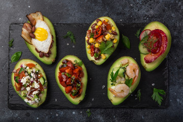  avocado halves stuffed with different toppings on dark background