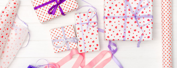 Flat lay of small gifts wrapped in patterned hearts gift wrap, scissors and silk ribbon. Ventine wrapping for holidays