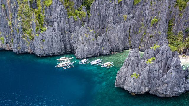 Aerial drone view of traditional boats in a narrow bay with a beautiful sandy beach and towering, jagged limestone cliffs