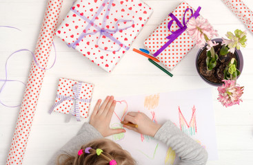 Little girl drawing happy mother's day greeting card with presents on the table. Mothers day background