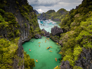 Aerial drone view of a beautiful tropical lagoon filled with kayaks and surrounded by jagged limestone cliffs (Small Lagoon, Miniloc Island, El Nido) - obrazy, fototapety, plakaty