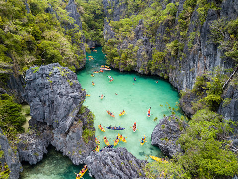 Aerial drone view of kayaks inside a beautiful shallow tropical lagoon surrounded by jagged cliffs and jungle (Small Lagoon, El Nido)