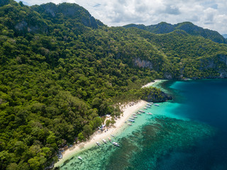 Aerial drone view of a small, tropical sandy beach and tourist boats over a coral reef