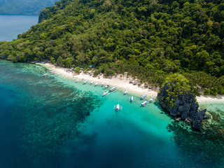 Fototapeta premium Aerial drone view of traditional Banca boats and coral reef surrounding a scenic tropical sandy beach (7 Commando Beach, El Nido)