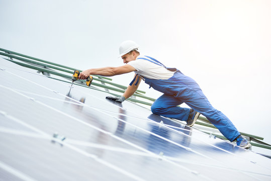 Construction worker connects photo voltaic panel to solar system using screwdriver. Professional installing and construction of solar system, alternative energy and financial investment concept.