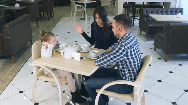 Indignant mother blaming on daughter and husband in cafe. Littke girl closing her ears.