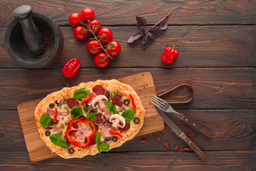 Homemade pizza with ham, pepperoni, mushrooms, capers and olives on a dark wooden table.