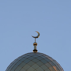 Fototapeta na wymiar The symbol of Islam is a golden crescent moon on top of the mosque minaret. Blue evening or morning sky. A square picture.