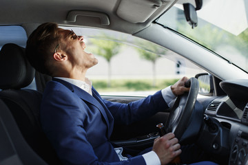 Happy businessman sits shows his emotions sitting at the steering wheel inside the car