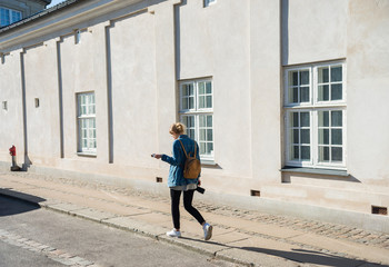 back view of young woman with camera walking on street in copenhagen, denmark