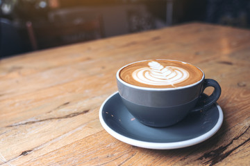 Closeup image of a blue cup of hot latte coffee with latte art on vintage wooden table in cafe