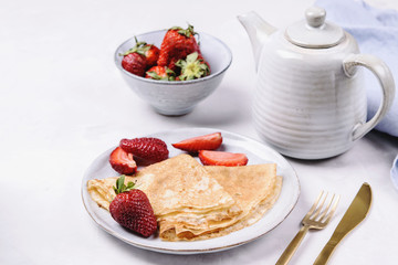 Openwork thin cheese crepes served with strawberry on grey concrete background. Homemade pancakes. Delicious breakfast