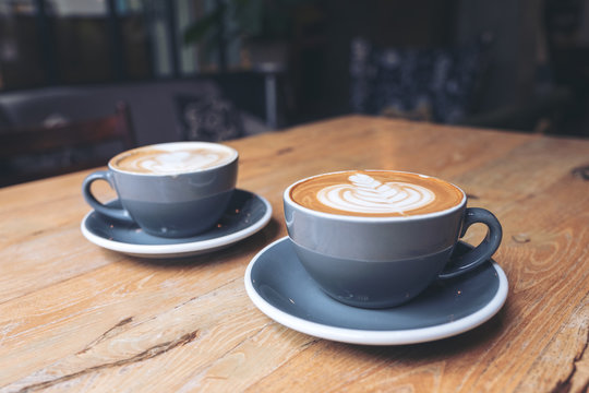 Closeup image of two blue cups of hot latte coffee on vintage wooden table in cafe