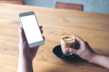 Mockup image of a woman holding white mobile phone with blank desktop screen and coffee cup in cafe