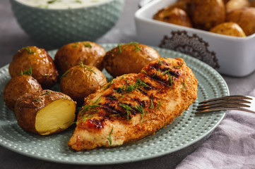 Grilled chicken fillet with baked potatoes and garlic yogurt dip.