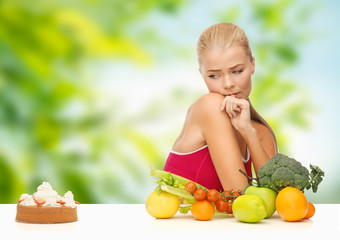 diet, junk food and eating concept - doubting woman with fruits and vegetables looking at cake over...