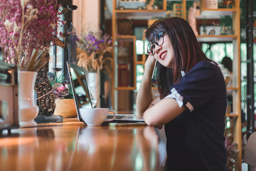 Asian business female working with laptop and make a note of something making notes on in coffee shop like the background.