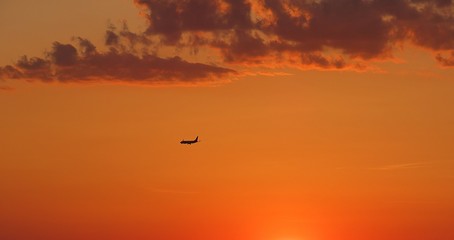 Naklejka na ściany i meble Airplane on beautiful orange fiery sunset background at sunset 