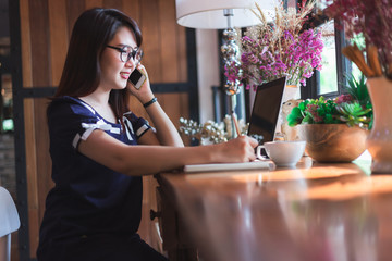 Business Asian woman hold pick up Smartphone working with laptop computer on in coffee shop like the background.