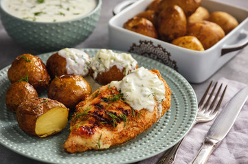 Grilled chicken fillet with baked potatoes and garlic yogurt dip.