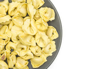 Raw tortellini pasta on a grey ceramic plate flatlay isolated on white background Italian traditional dumpling.