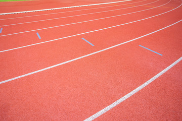 Fototapeta premium White lines of stadium and texture of running racetrack red rubber racetracks in outdoor stadium are 8 track and green grass field,empty athletics stadium with track.
