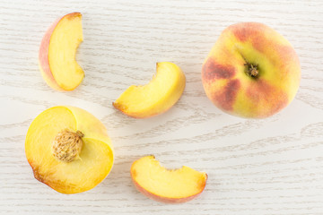 One yellow peach, a section half and three slices, flatlay, on grey wood background.