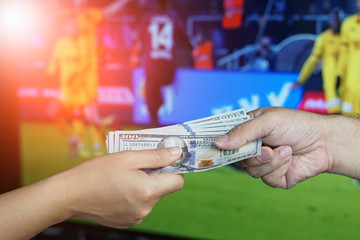 Football Gambling Concept : Hand gives money to another over TV screen showing football match as background.