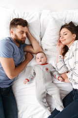 Cute young family. Parents lies on bed with their little child.