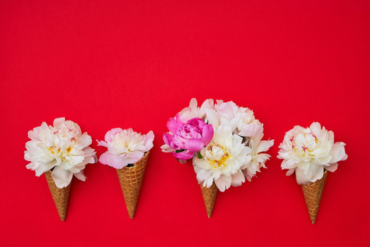 Ice cream cones with white peony flowers on red background. Summer concept. Copy space, top view. Red summer background
