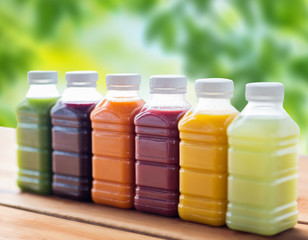 healthy eating, drinks, dieting and packaging concept - plastic bottles with different fruit or vegetable juices on wooden table over green natural background