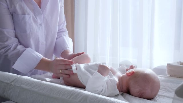 child hygiene, woman rubs baby ass with napkin and changes diaper on table in natural light near window