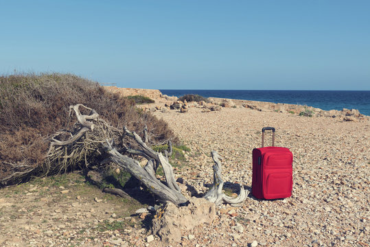 Red suitcase on a rocky sea shore at Cap de ses Salines in Majorca. Selective focus