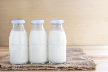 Three full bottles of milk placed on sackcloth on a wooden table.