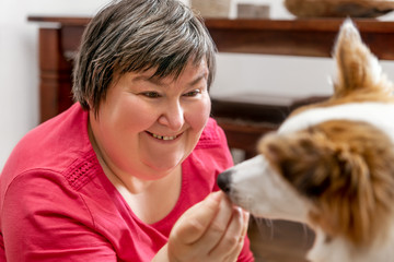 Geistig behinderte Frau gibt Hund ein Leckerli, Konzept tiergestütze Therapie