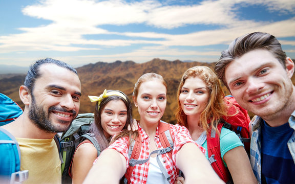 technology, travel, tourism, hike and people concept - group of smiling friends with backpacks taking selfie over grand canyon national park hills background
