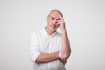 Close up portrait of handsome mature man in white shirt holding hand near face and thinking about...