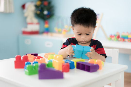 Adorable Asian Toddler baby boy sitting on chair and playing with color block toys at home..